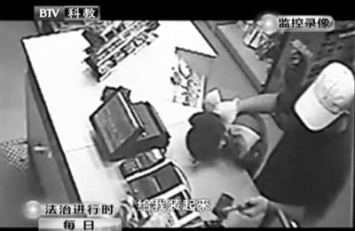 戴帽男子一手掐住加油站營(yíng)業(yè)員，一手持發(fā)令槍指向另一營(yíng)業(yè)員，要求“把錢(qián)給我裝起來(lái)”。