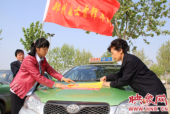 　　授旗結(jié)束后，首都的士雷鋒車隊(duì)王鳳進(jìn)隊(duì)長（右）與鄭州的的哥的姐在車身上貼上標(biāo)識。