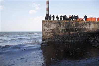 昨日，山東青島，清污人員正在海邊清理油污。