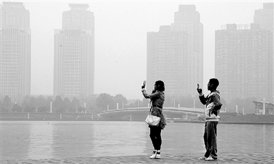 29日中午，鄭東新區(qū)如意湖畔，兩個年輕人拍攝霧霾中的景色。 鄭州晚報記者 馬健 圖
