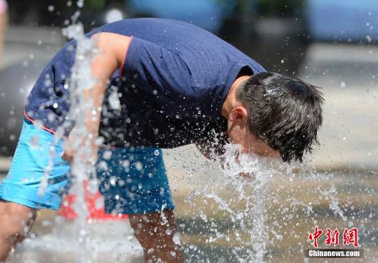 5月29日，一名小孩將頭伸向北京街頭的噴泉以降溫祛暑。