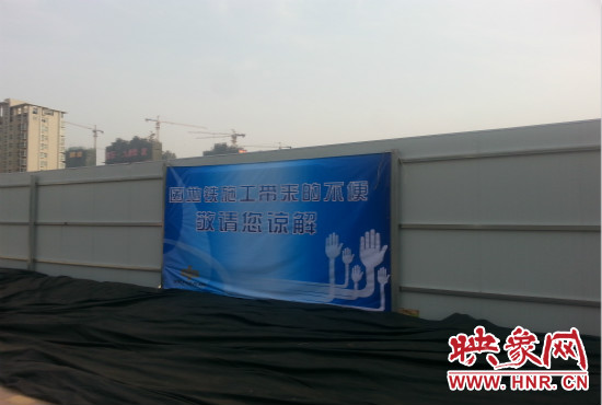 道路南側(cè)圍起了白色的圍擋，墻上標示著“因地鐵施工帶來的不便敬請您諒解”的提示牌。