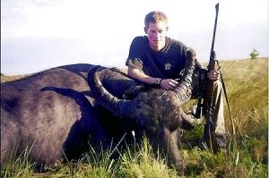 哈里王子手持獵槍，蹲在一頭遭到獵殺的水牛旁邊